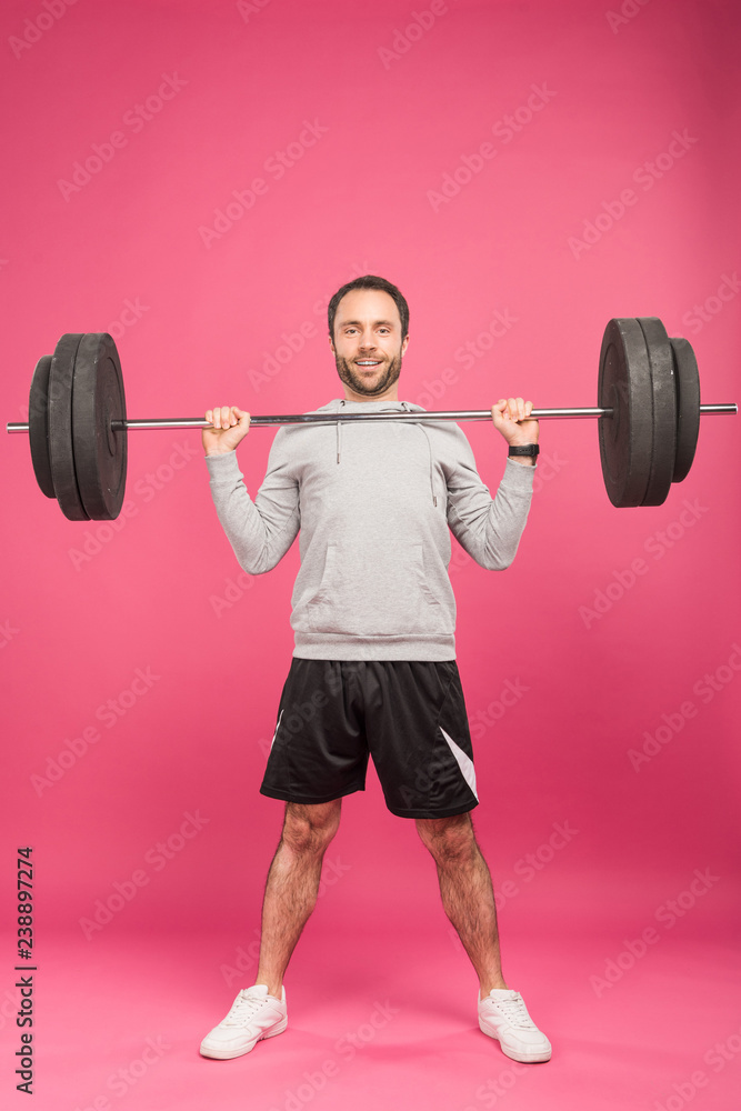 handsome sportsman exercising with barbell, isolated on pink handsome sportsman exercising with barbell, isolated on pink