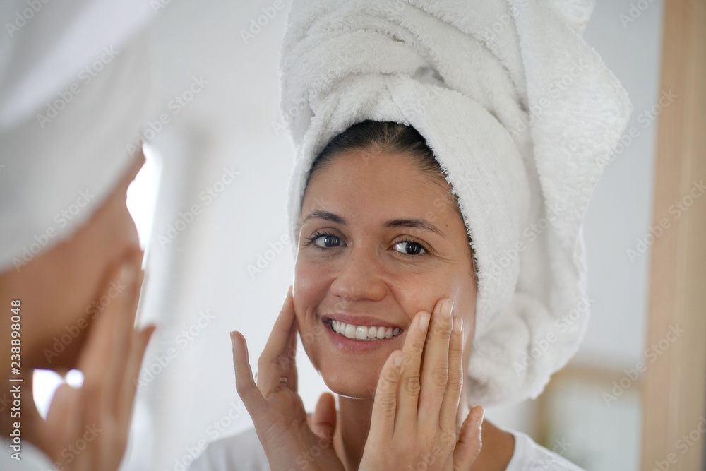 Beautiful brunette in towel turban looking at face in mirror Beautiful brunette in towel turban looking at face in mirror
