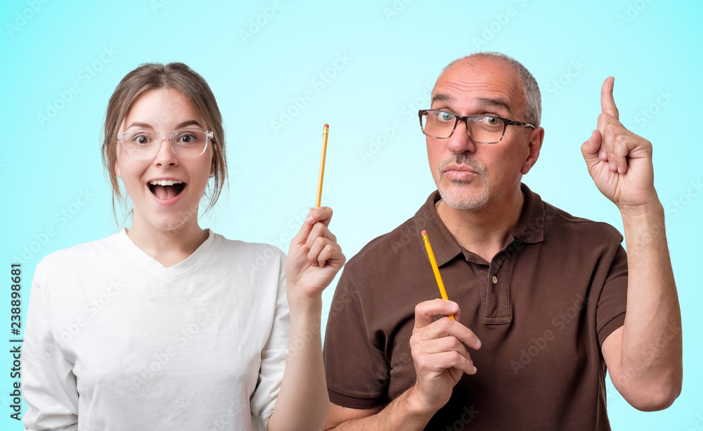 Female caucasian student in glasses and white t-shirt and senior teacher pointing an idea looking very excited standing on bright blue background. Concept of studying in college or university Female caucasian student in glasses and white t-shirt and senior teacher pointing an idea looking very excited standing on bright blue background. Concept of studying in college or university