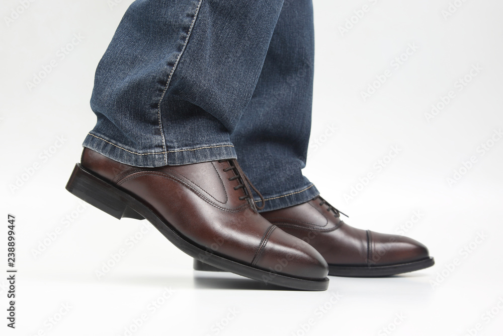 Male legs in jeans and brown classic shoes on white background