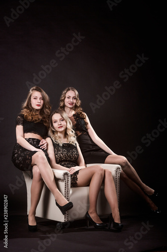 Three beautiful girls in black evening dresses are sitting in the chair