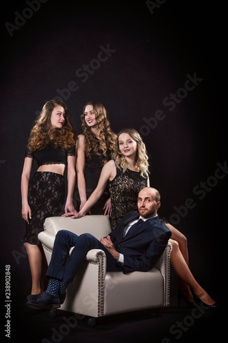 Portrait of a man sitting in a chair and surrounded by beautiful girls in black evening dresses