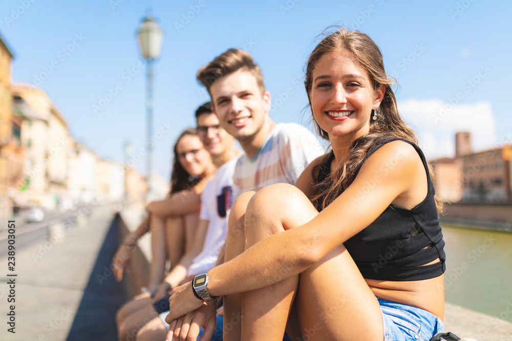 Italy, Pisa, group of four happy friends sitting on a wall along Arno river