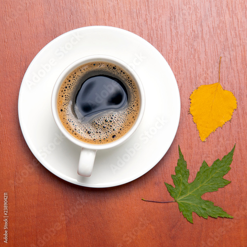 White cup with black coffee and autumn leaves