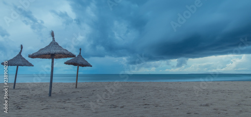Mallorca, Balearic Islands, Spain - October 28, 2018: Three umbrellas on a lonely beach under a stormy sky
