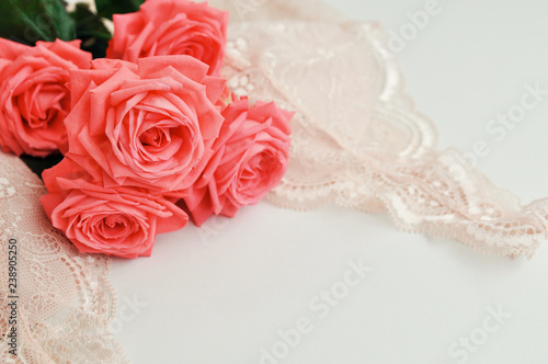 Delicate feminine theme. Pink coral roses trend color on a pale pink bra and pearl necklace on a white background. top view. close up. Stylish lingerie flat lay. selective focus