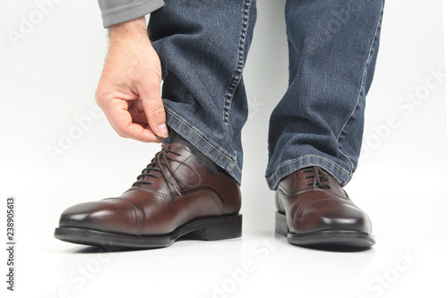 man straightens his shoelaces on brown classic shoes on a white background