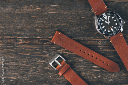 Brown leather handmade watch strap on mens luxury watch laying on dark rustic wooden table. Close Up. Copy space.