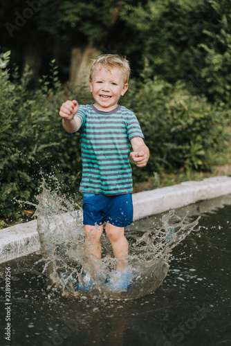 Fototapeta Naklejka Na Ścianę i Meble -  little boy jumping in a puddle in summer