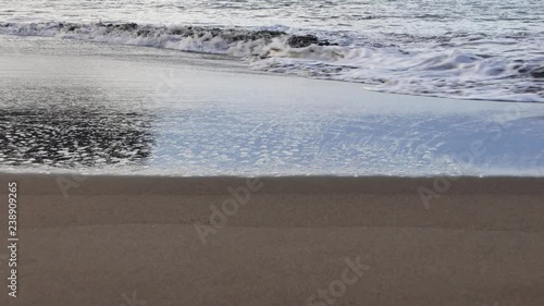 Soft and delicate waves flowing on smooth sandy coast.