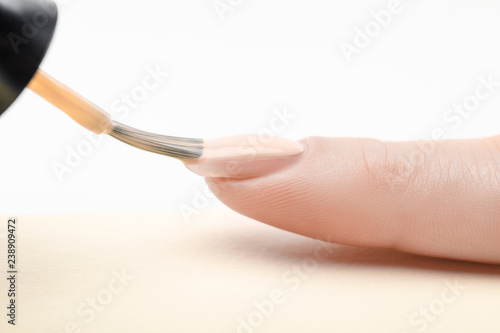 ivory nail polish on fingernail of woman with wet brush on white background