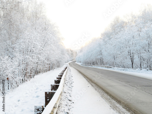 Beautiful winter road running through the snowy woods. White trees in the snow. The road stretches into the distance.