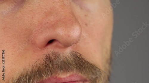 man with mustache sniffles by nose and wipes it with his fingers, gray background, close-up 