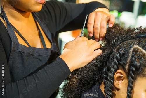 Close up african hairstylist braided hair of afro american female client in the barber salon. Black healthy hair culture and Style. Stylish therapy professional care concept. Selective focus. © okrasiuk