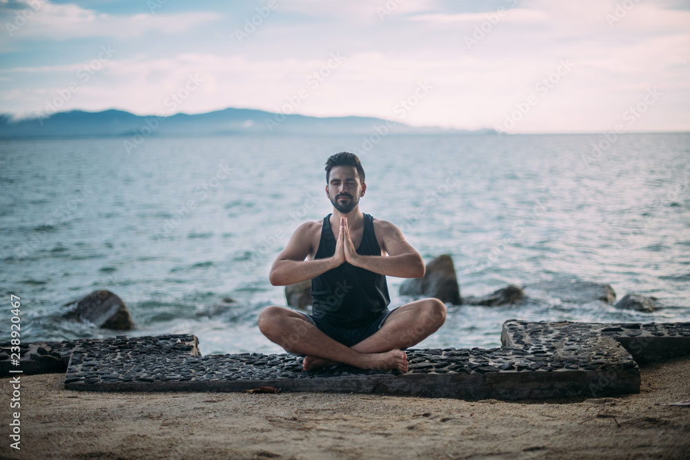 Young man doing yoga by the sea. A handsome guy is sitting on the ocean at sunset.