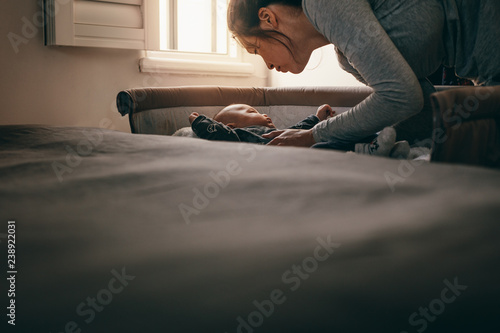 Photography Mother putting her baby in a bedside baby crib