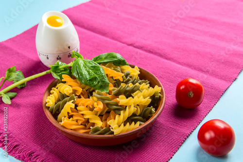 Uncooked Italian Fusilli Pasta with kitchen timer, tomatoes and basil