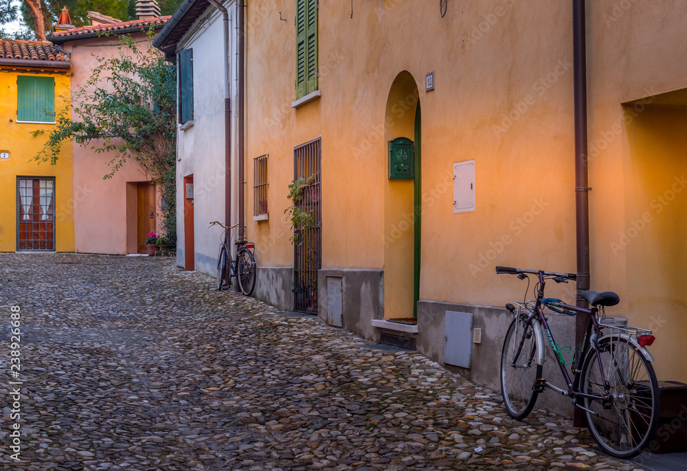 Bicycles next to a yellow walled house in a lovely small street along the city walls of medieval Cesena in Italy