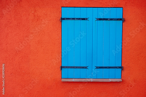 Blue wooden closed shutters on window on orange wall, copy space