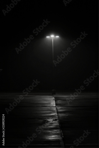 Street lamp on dark night, deserted film noir black and white mystery shadows eerie minimalist copy space vertical format.