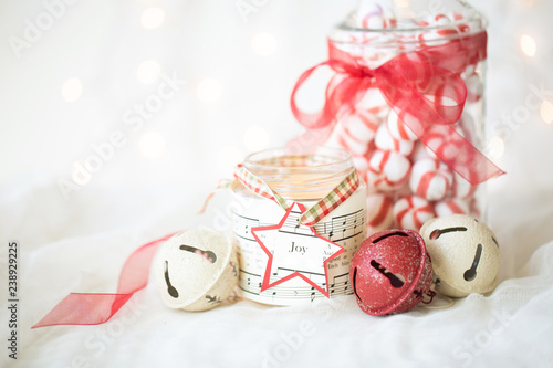 Christmas photograph of red peppermint candies  a jar candle  and red and cream sleigh bells with twinkle lights