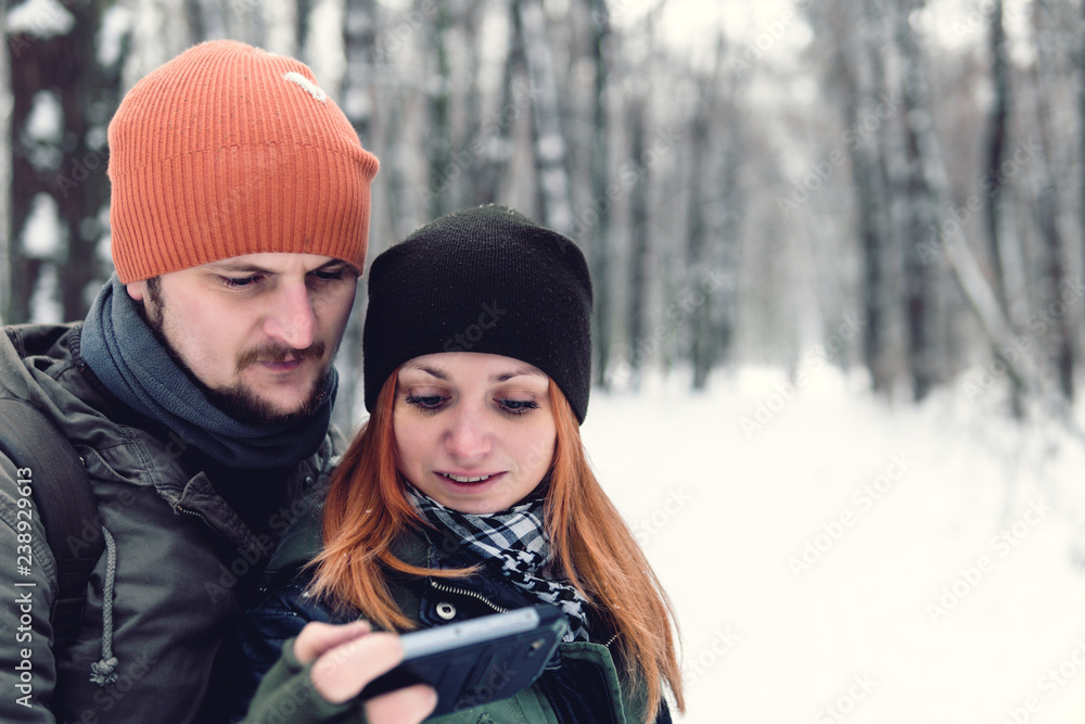 Close up portrait. Couple watching videos in a smart phone on winter holidays with the snowy forest in the background. use smartphone, copy space. Serious look Close up portrait. Couple watching videos in a smart phone on winter holidays with the snowy forest in the background. use smartphone, copy space. Serious look