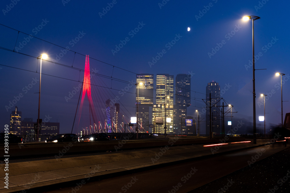Rotterdam night time cityscape of the Erasmus bridge and skyscraper buildings with the lights of traffic passing by