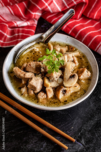Soup with pieces of pork and mushrooms in bowl.