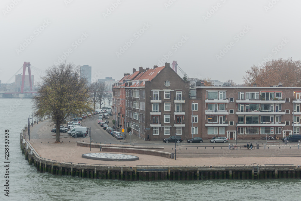 Neighbourhood quay in the city centre of Rotterdam on a hazy overcast day with in the background a bridge and city constructions