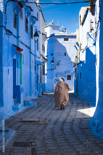 A man with a traditional dress is walking in the beautiful blue medina of Chefchaouen, Morocco. © Travel Wild