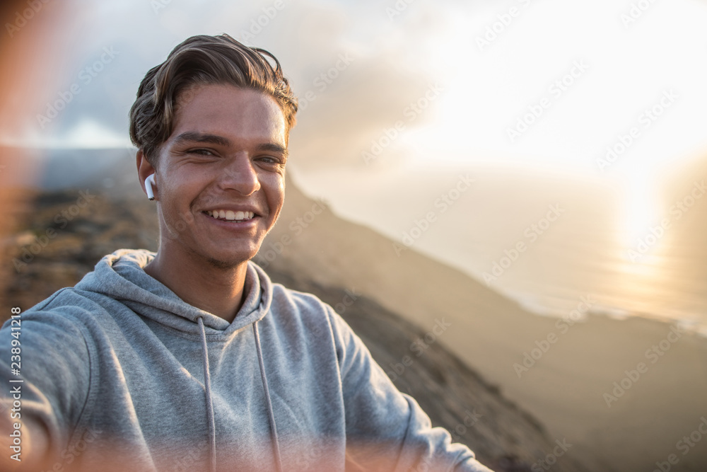 Happy young handsome guy, making selfie portrait on a mountain hill in sunset light. Happy young handsome guy, making selfie portrait on a mountain hill in sunset light.