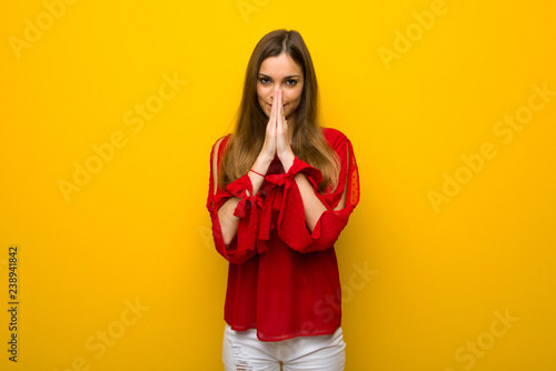 Young girl with red dress over yellow wall keeps palm together. Person asks for something