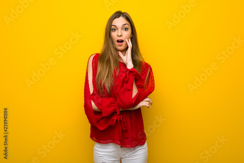 Young girl with red dress over yellow wall surprised and shocked while looking right