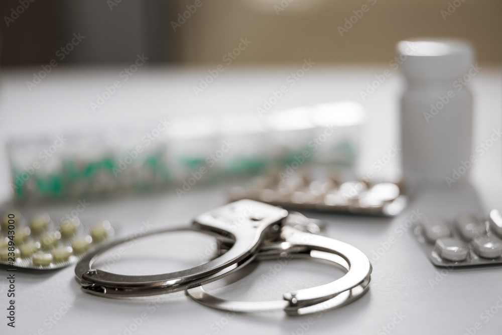 Handcuffs and pills and drugs on white table. Handcuffs and pills and drugs on white table.