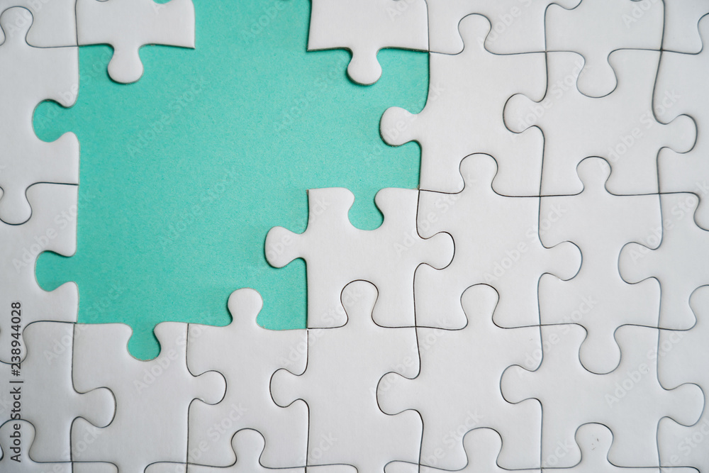 Fragment of a folded white jigsaw puzzle and a pile of uncombed puzzle elements against the background of a colored surface.