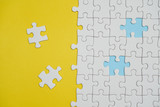 Fragment of a folded white jigsaw puzzle and a pile of uncombed puzzle elements against the background of a yellow surface.