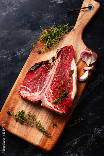 T bone of beef with spices on a wooden board and black background. Raw dry aging steak 3 months.