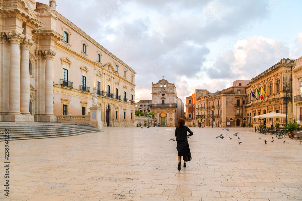 Young woman is running across the main square with pigeons, island of Ortigia, Syracuse, Italy