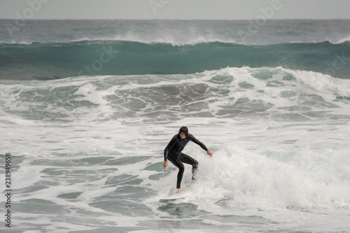Brunette guy in the black swimsuit riding on a surf on the sea