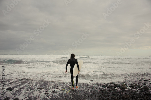 Brunette man in the black swimsuit with a surf in his hands walking to the sea