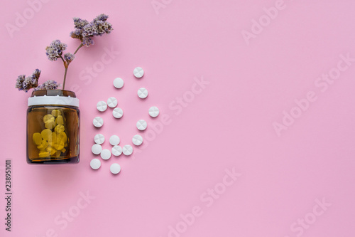 A bottle of medicines and scattered pills on a pastel pink background. Ripped vitamins on a bright background. healing herbs. photo
