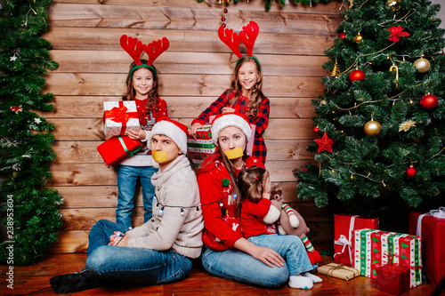 Bad kids and father and mother tied up with garland near Christmas tree at home © Elena Kratovich