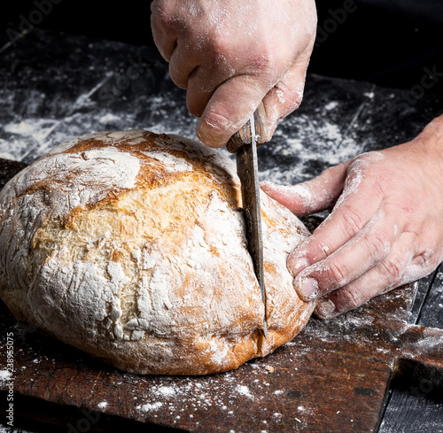 male hands cut a knife round baked bread