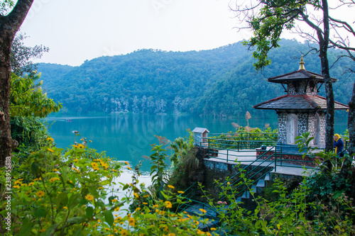 Green shore of lake Fewa, Pokhara. Small hindu temple and flowering trees.