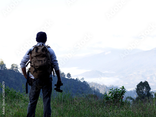 Young man with backpack and holding a binoculars standing on top of mountain