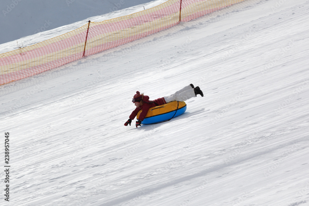 Young girl downhill on snow tube on ski resort at sunny winter day