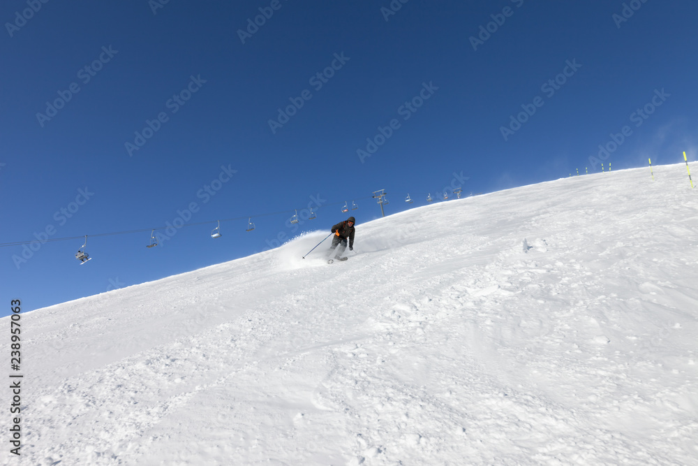 Skier descends on snowy ski slope in sunny winter day.