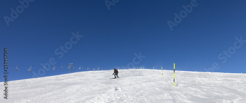 Snowy ski slope with skier and sk-lift at sunny winter day