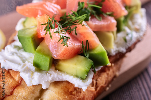 Delicious and healthy homemade sandwich with creamy cheese and slices of avocado and trout (salmon) are on a wooden board and ready to eat, macro