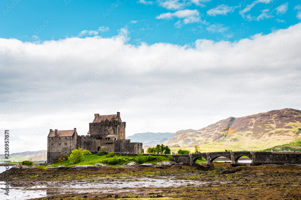 Eilean Donan Castle in the Highlands of Scotland on a cloudy day and low tide, ancient castle with sandstone bridge, lush nature with colorful moss and lichens 